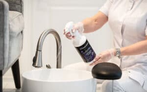 Spa professional preparing Prevention Disinfectant Spray beside a pedicure basin