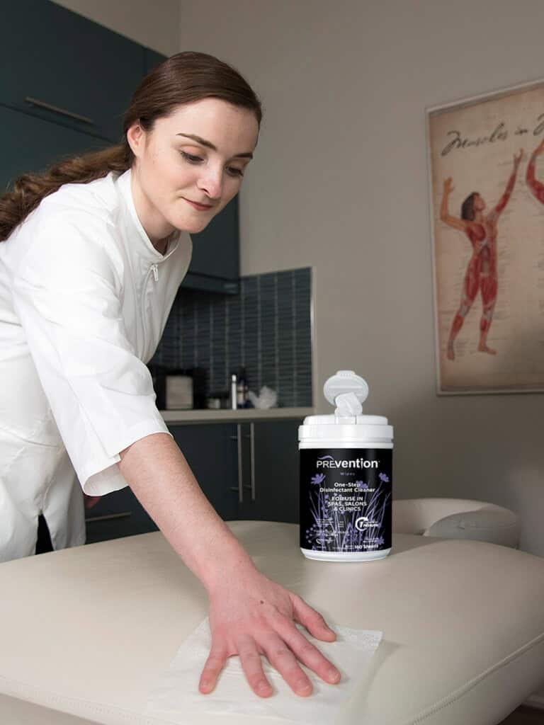 Massage therapist disinfecting massage table with Prevention Wipes